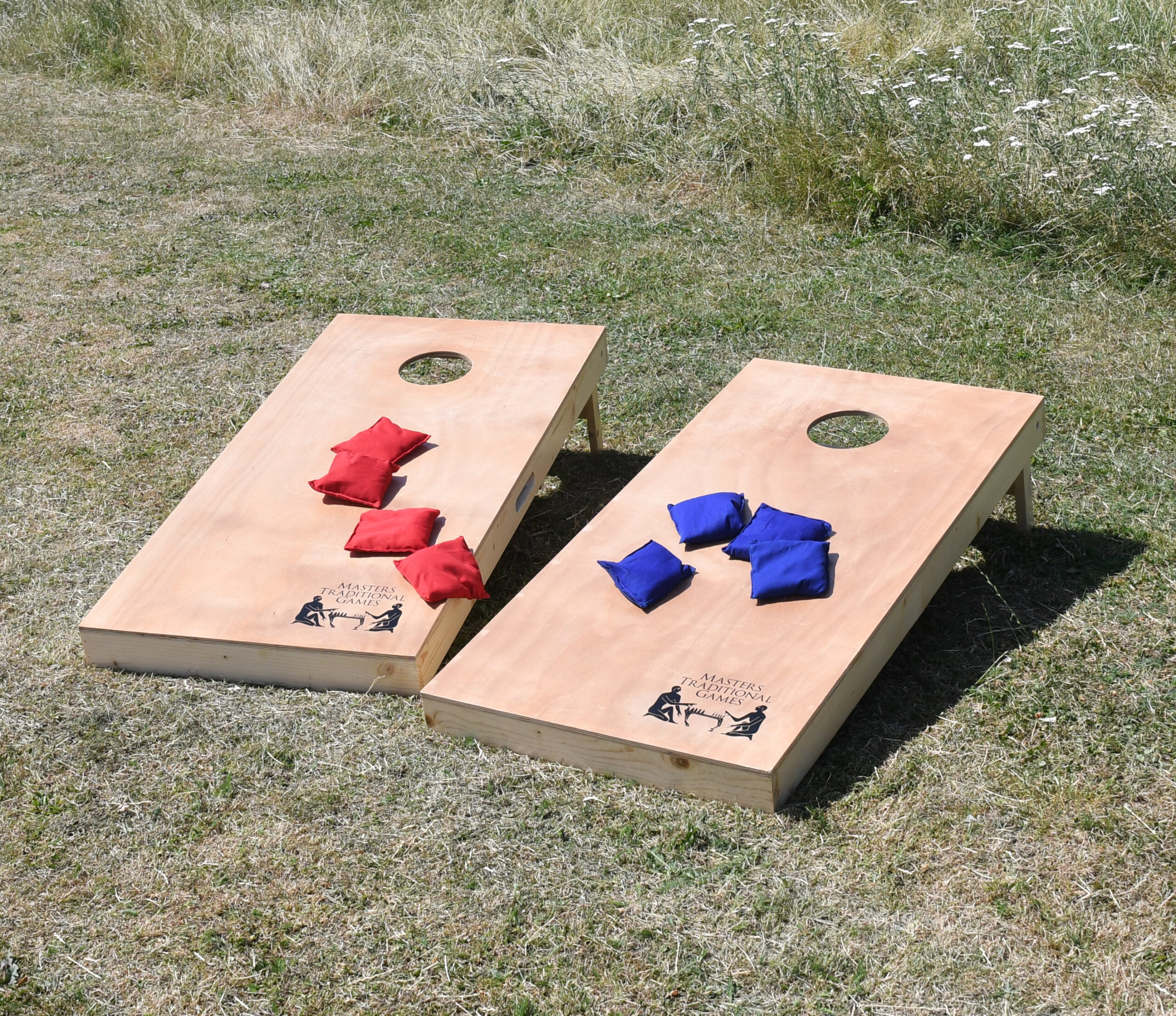 masters-cornhole-1 - Masters Traditional Games - Masters Traditional Games Two cornhole boards on grass with red and blue bean bags ready for play outdoors.