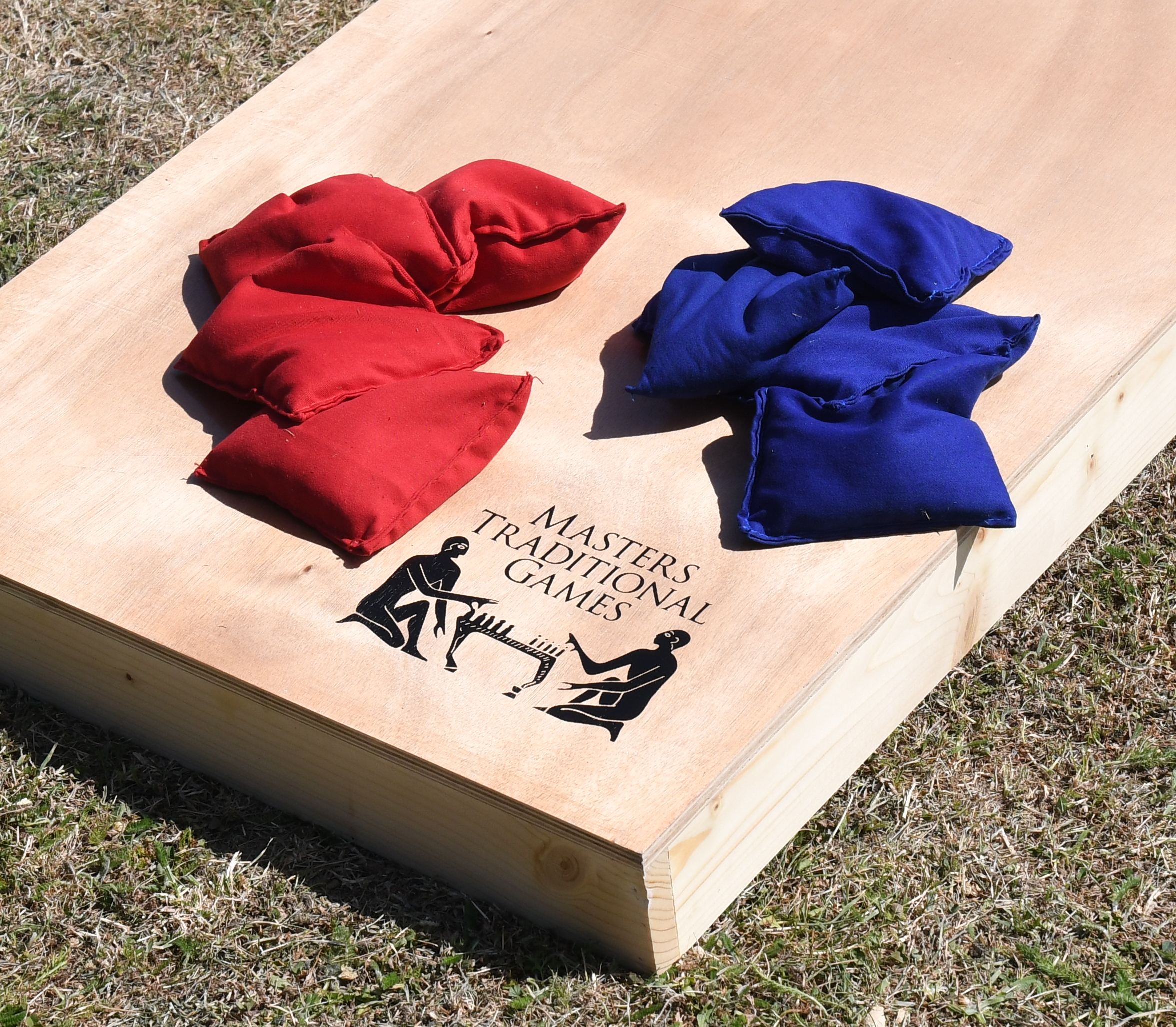 masters-cornhole-11 - Masters Traditional Games Red and blue fabric bean bags resting on a light wooden game board outdoors on grass.