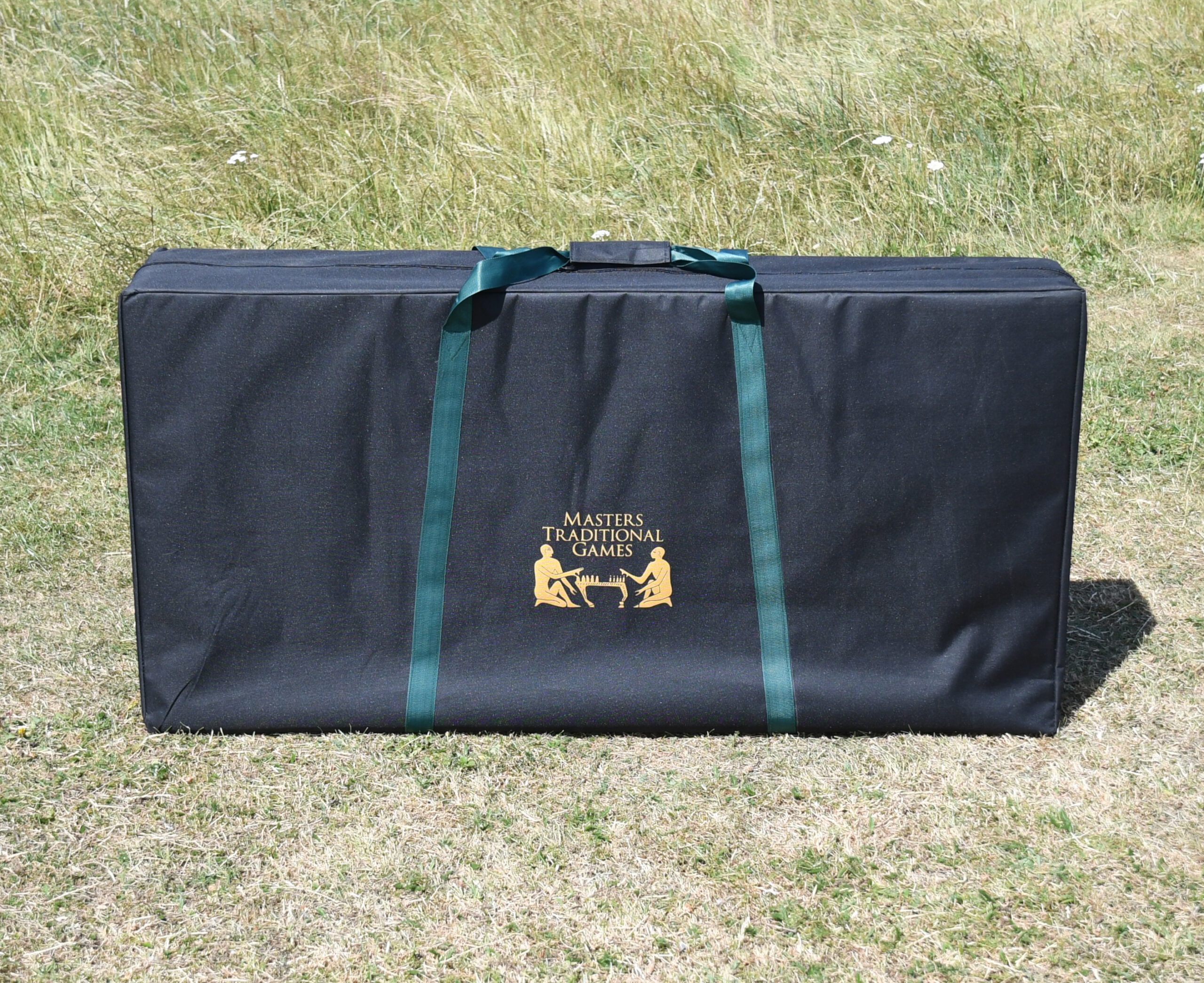 masters-cornhole-2 - Masters Traditional Games Large black carrying case with green straps and a gold logo reading Masters Traditional Games on a grassy field.