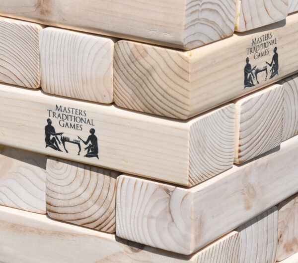 masters-giant-wooden-tumble-tower-11 - Masters Traditional Games Stacked wooden blocks with a printed logo reading 'Masters Traditional Games' and silhouettes of people playing chess on the side.