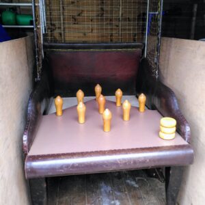 Indoor view of a wooden pin-setting machine: several wooden bowling pins stand on a brown lane inside a small, enclosed trough with netting behind.