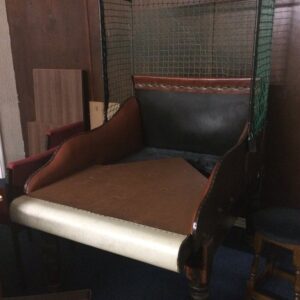 Vintage upholstered chair with a tall green wire cage-like frame attached behind it in a dim room.