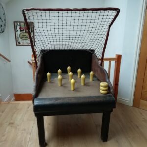 Leather chair with a metal grid net above its back, placed indoors, with yellow game pegs arranged on the seat and a few stacked on the right edge of the seat.