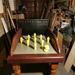 Vintage wooden peg game with yellow pegs on a green board inside a cluttered workshop.