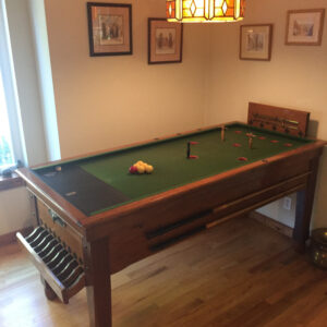 sams-bar-billiards-table-2020-ca-1 - Masters Traditional Games - Masters Traditional Games Pool table in a wood-furnished room with a Tiffany-style hanging lamp overhead and framed pictures on the wall behind it.
