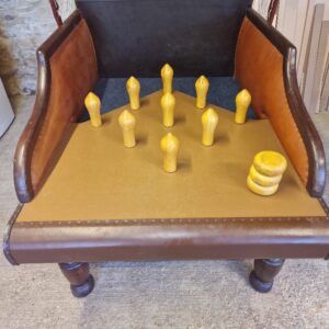 Vintage leather chair repurposed as a bowling-style game: nine yellow pins stand upright on the seat with a small stack of yellow discs at the side.