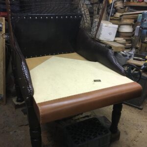 A partially assembled vintage-style leather armchair on four legs in a cluttered woodworking shop.