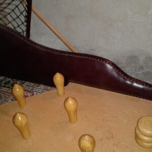 Wooden peg-board game on a leather-edged table with several pegs standing upright and a stack of wooden discs nearby.