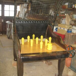Antique peg-board arcade game with yellow pegs on a wooden table in a cluttered workshop.