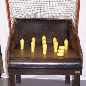 Old wooden chair with a netted back; on the seat are yellow toy bowling pins arranged for a playful game setup.